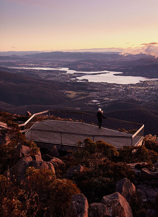 A woman standing on a wooden lookout platform looking over the city of Hobart.